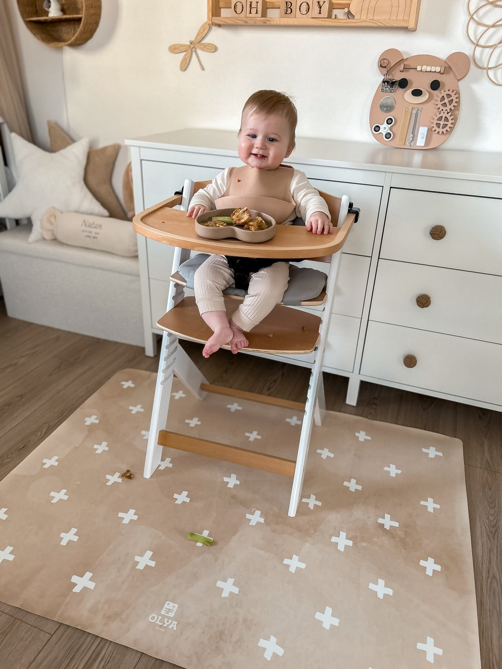 9. Smiling baby in high chair on beige OLYA KIDS floor mat with cross pattern, in nursery setting
