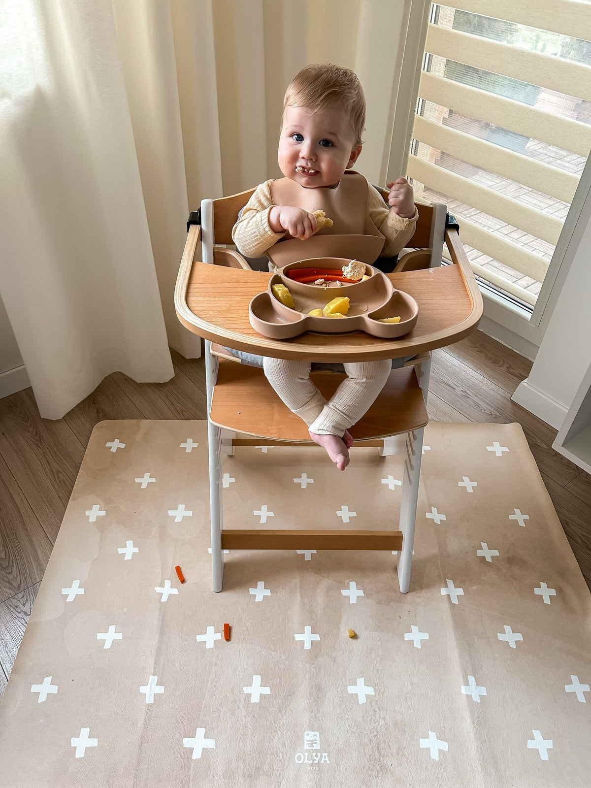 6. Baby in high chair on beige OLYA KIDS floor mat with cross pattern, eating snacks, near window