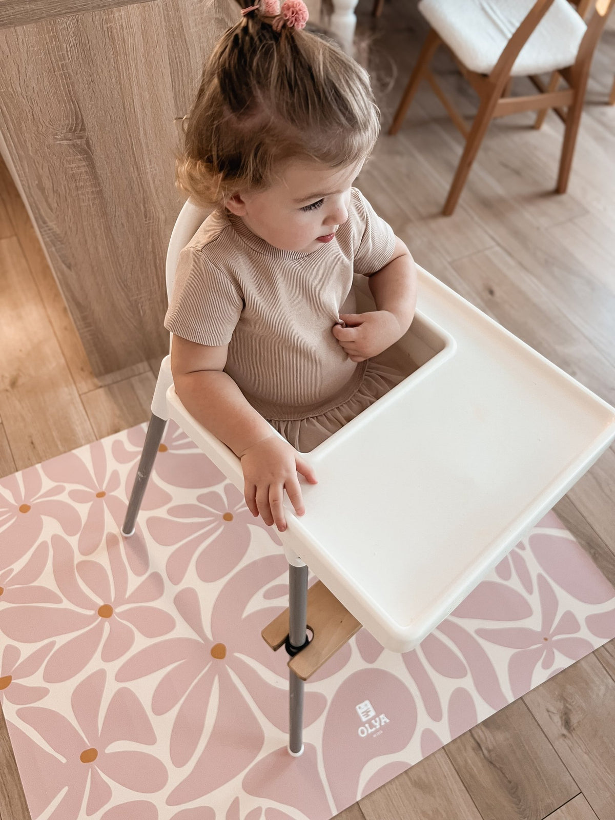 6. Child in high chair with pink daisy-patterned OLYA KIDS floor mat on wooden floor