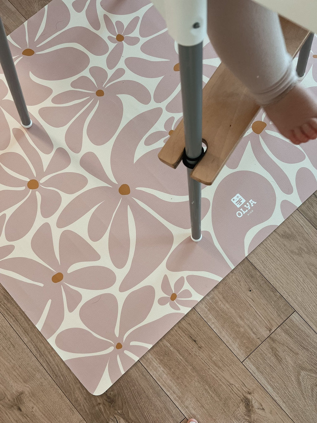 1. Child in high chair with pink daisy-patterned OLYA KIDS floor mat on wooden floor