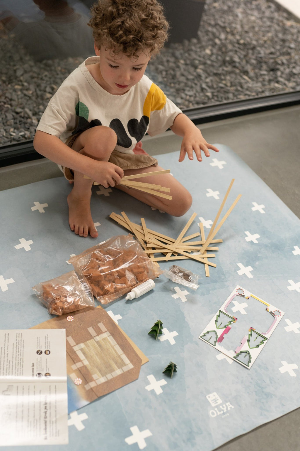 5. Child playing with craft materials on blue OLYA KIDS floor mat with white cross pattern, indoors