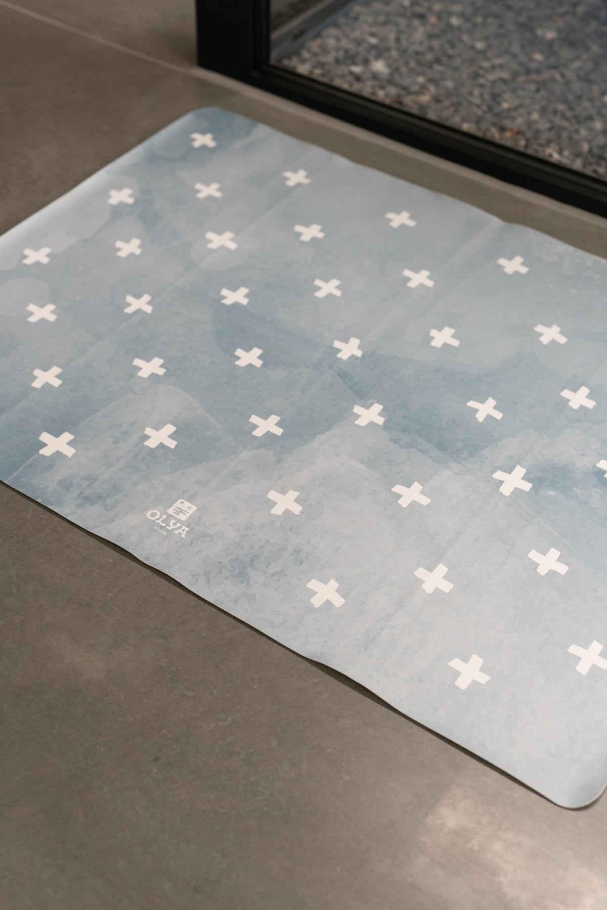 7. Blue OLYA KIDS floor mat with white cross pattern on concrete floor, near window