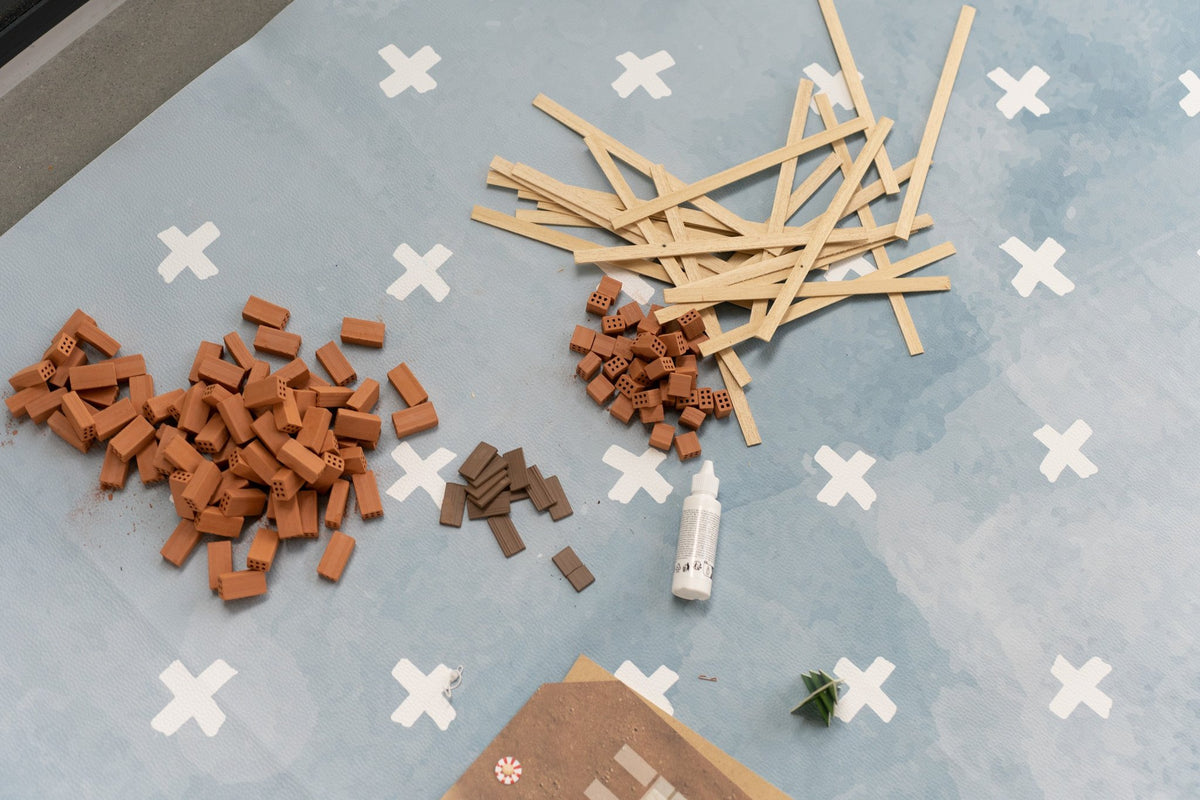 8. Close-up of craft materials on blue OLYA KIDS floor mat with white cross pattern