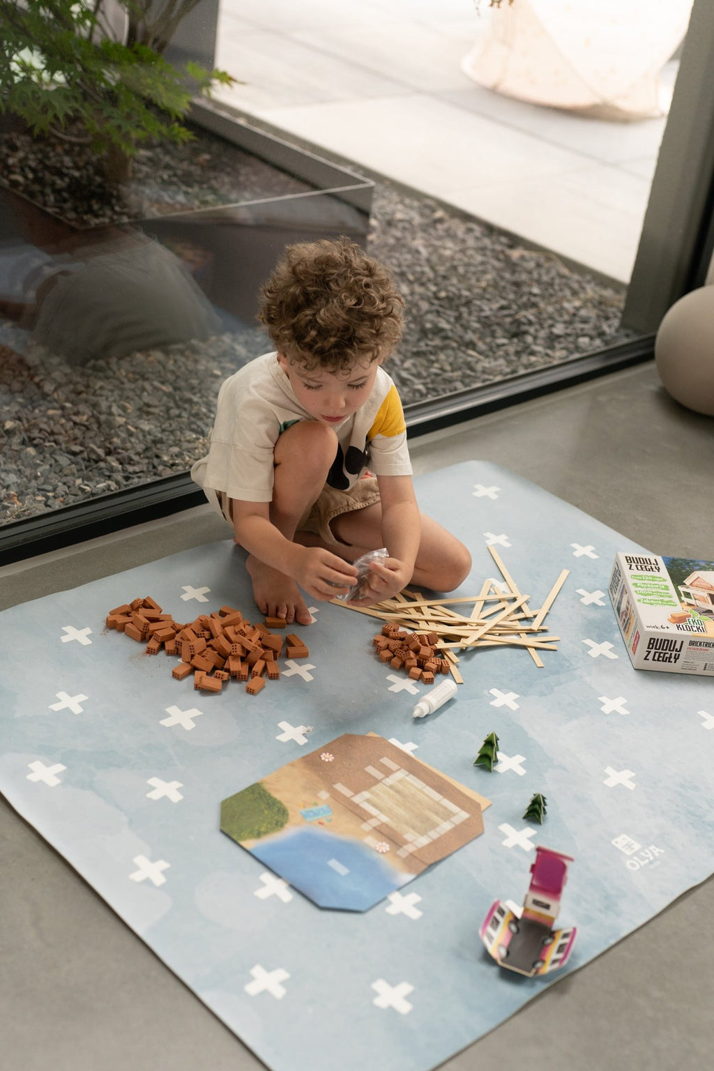 4. Child engaged in craft activity on blue OLYA KIDS floor mat with white cross pattern, indoors