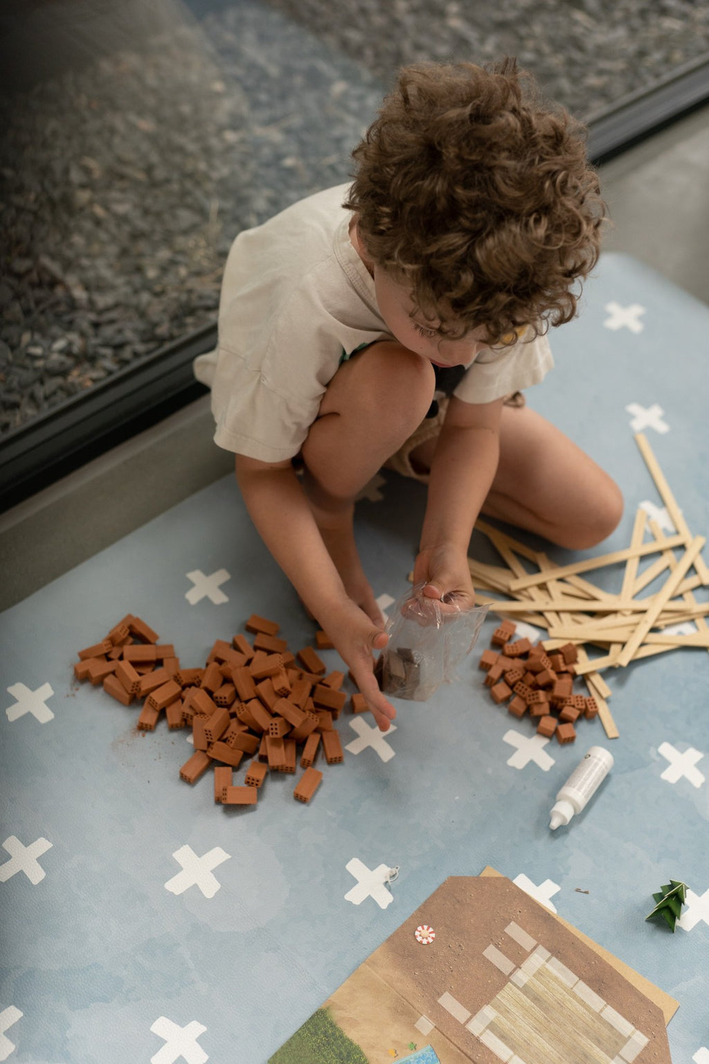 1. Child playing with building blocks on blue OLYA KIDS floor mat with white cross pattern, indoors
