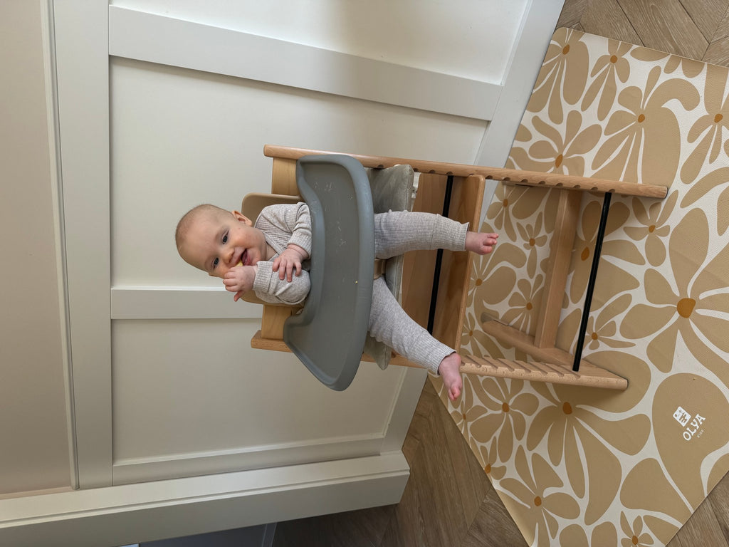 1. Baby in high chair on beige daisy-patterned OLYA KIDS floor mat against white wall
