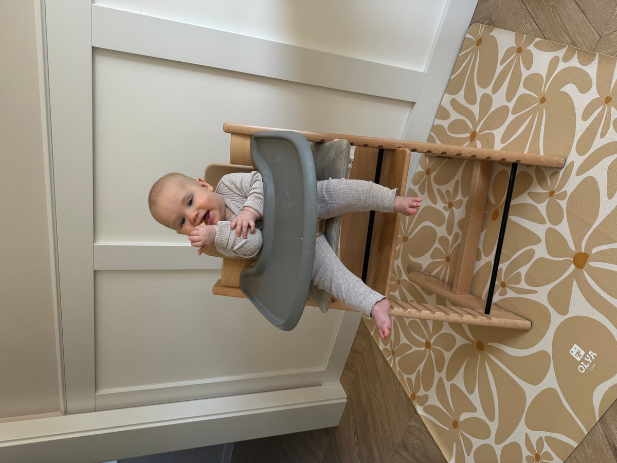 1. Baby in high chair on beige daisy-patterned OLYA KIDS floor mat against white wall
