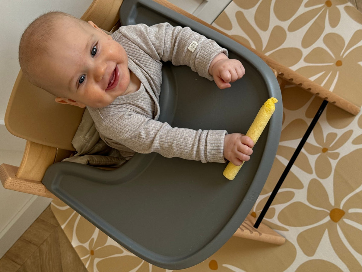 1. Baby smiling in high chair on beige daisy-patterned OLYA KIDS floor mat