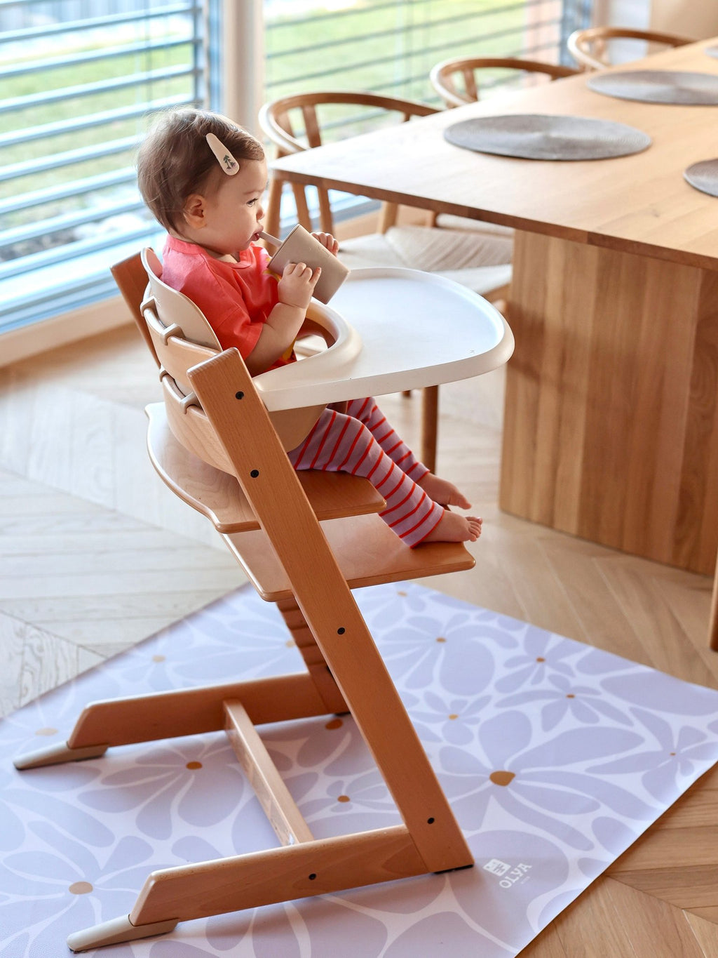 5. Baby in high chair with lavender daisy-patterned floor mat in bright dining area