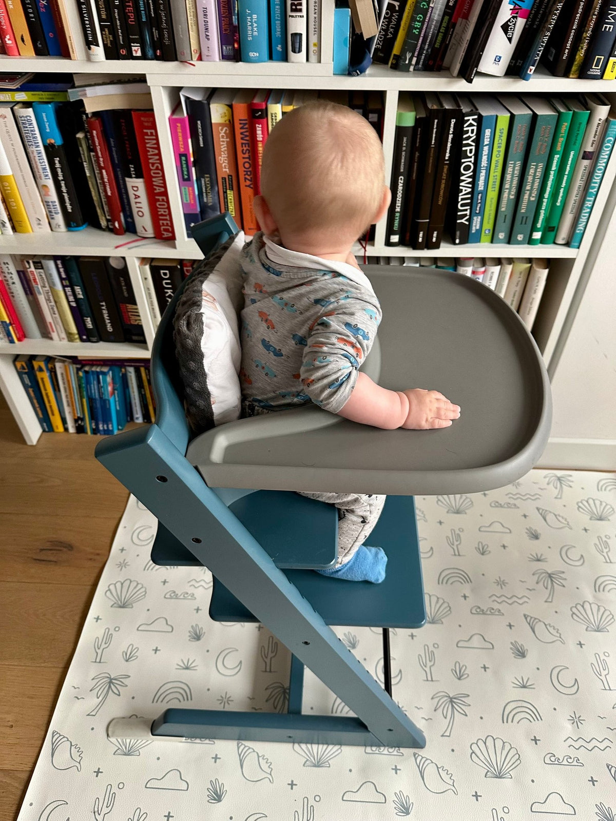 1. Baby in high chair on OLYA KIDS Palm Beach Azure floor mat with beach-themed patterns