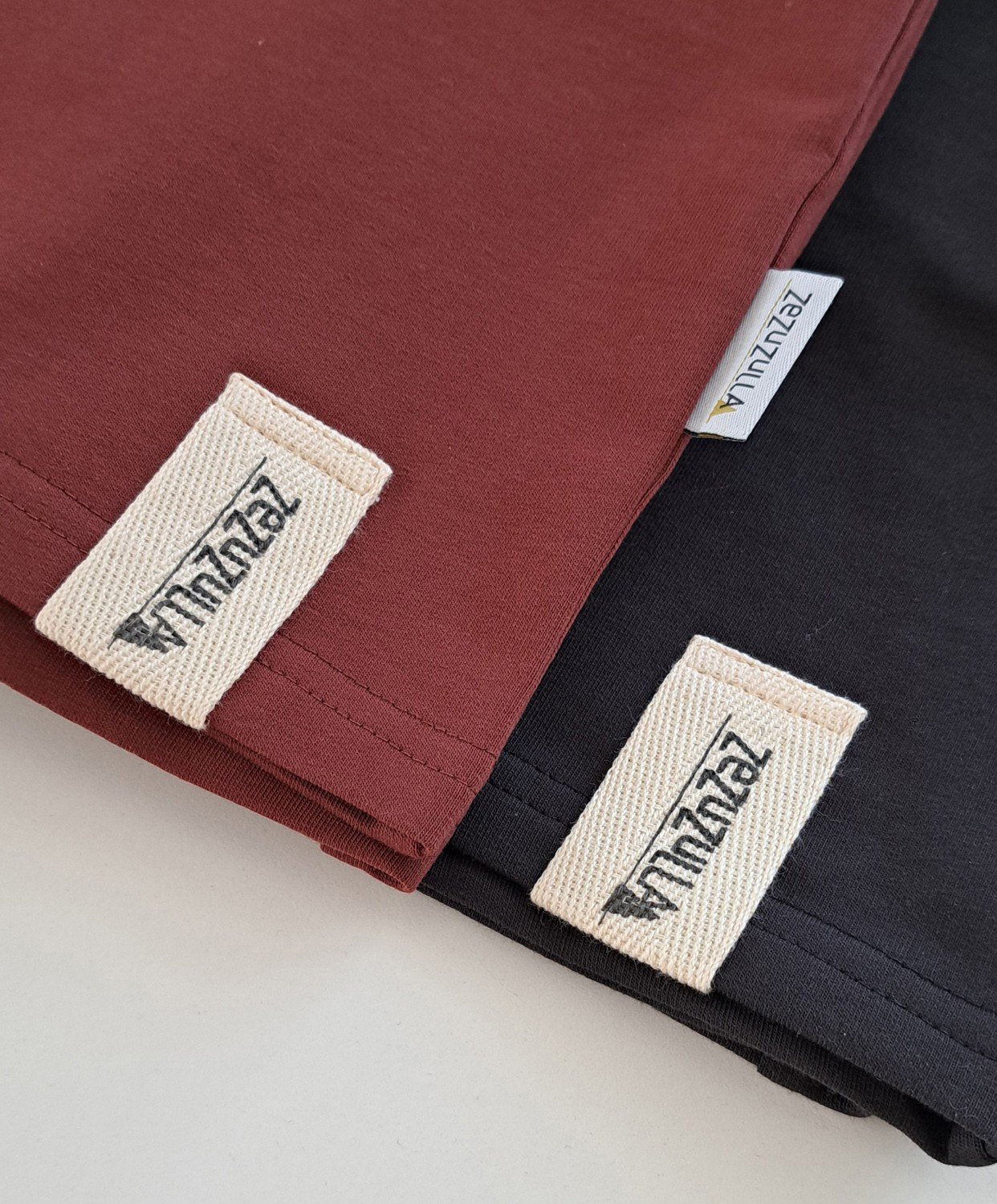 3. Close-up of Zezuzulla labels on dark antrachite and maroon cotton shorts, highlighting fabric texture and brand tag