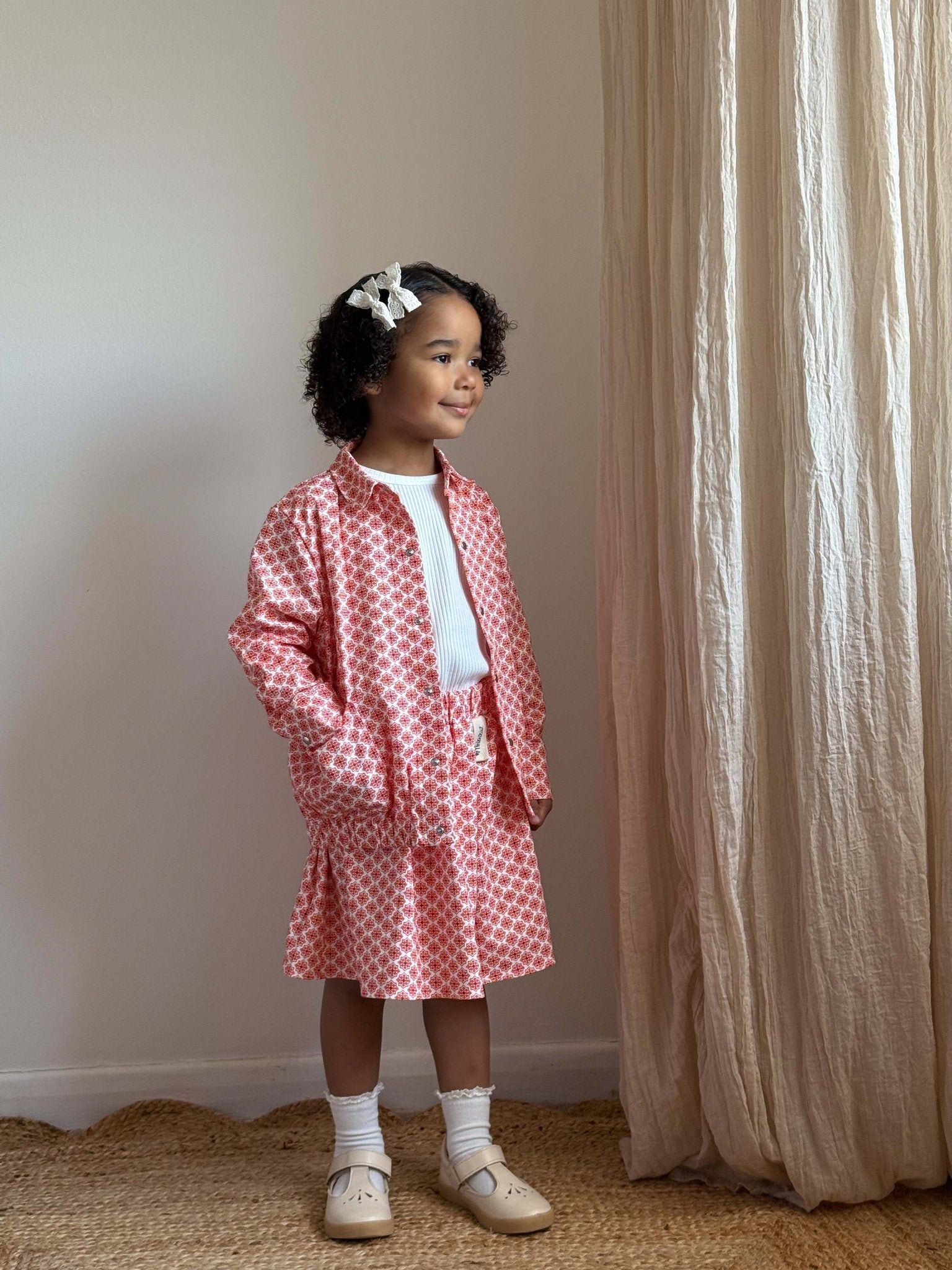 1. Young girl standing in room wearing Zezuzulla red and white skirt and jacket with white shirt and bow