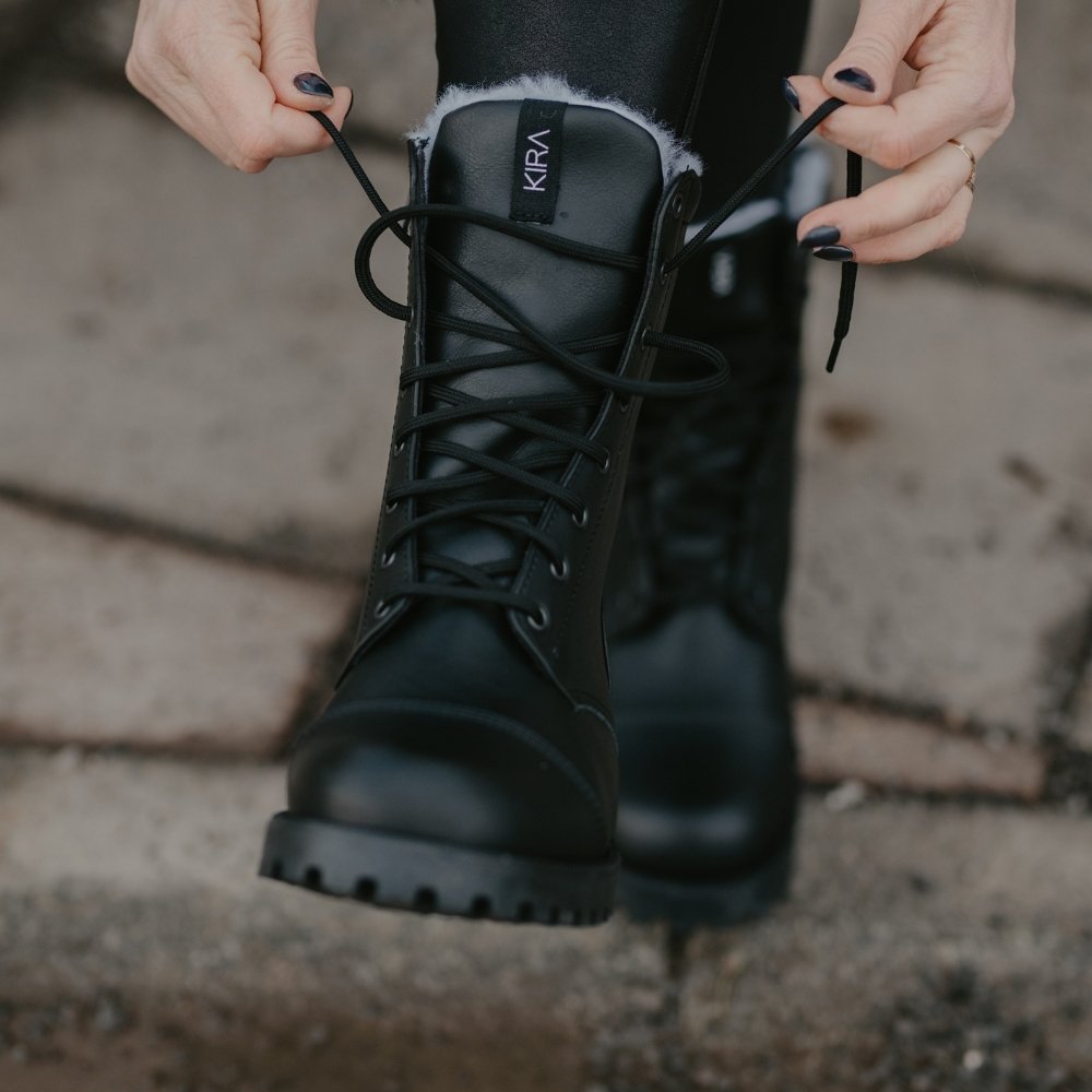 2. Woman tying laces of KIRA 4.0 black boots with vegan wool lining, shown outdoors