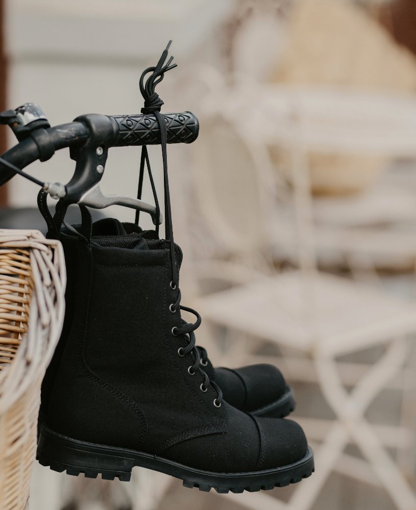 4. KIRA 5.0 black boots hanging from a bicycle handle, showcasing vegan-friendly design