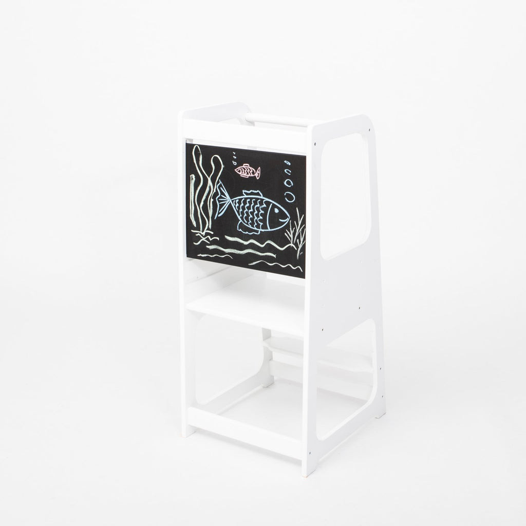 2. White Montessori kitchen helper tower with blackboard panel featuring fish drawing, shown in a studio setting