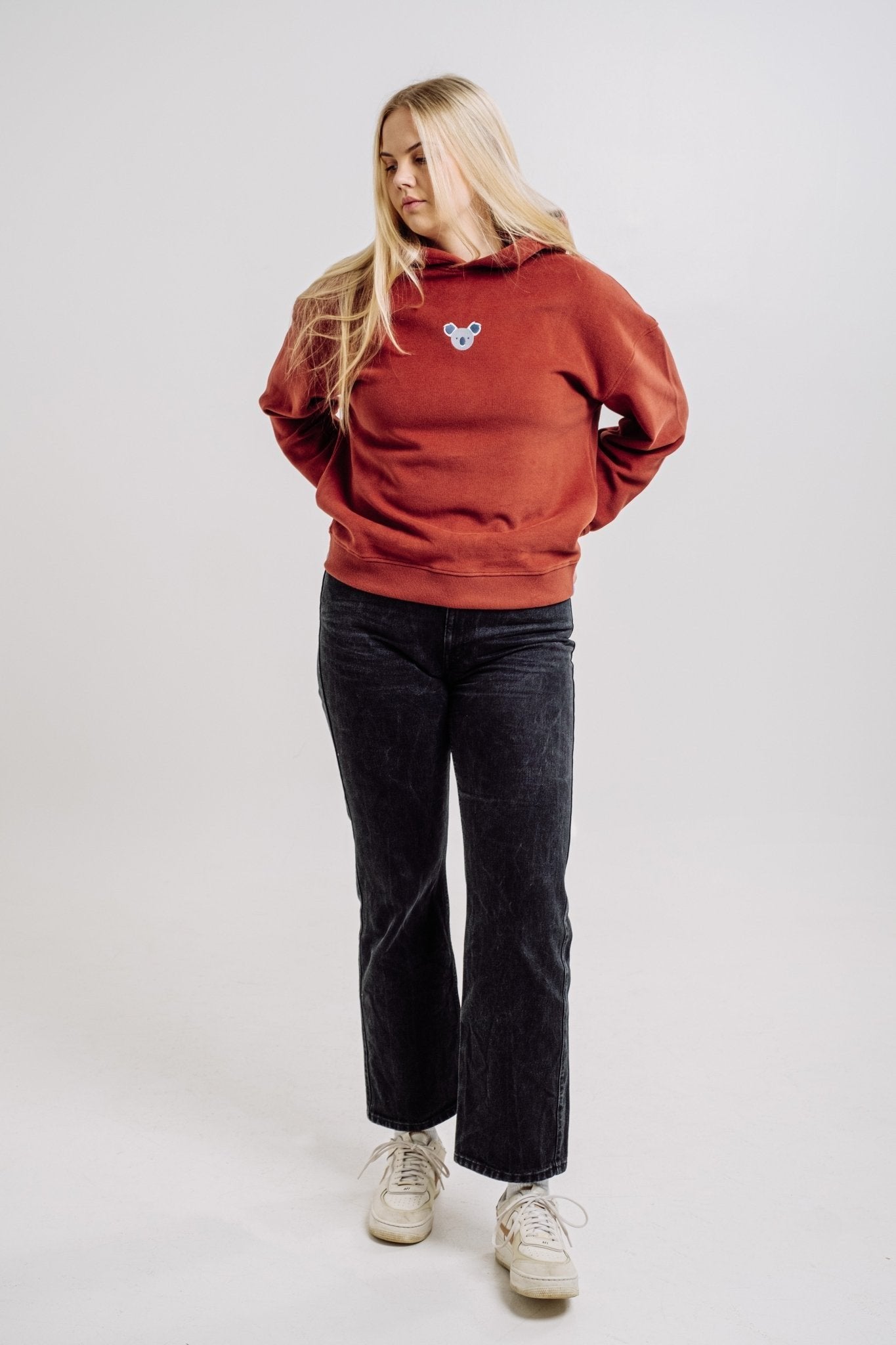4. Woman in Sossu Koala Hoodie in terracotta, standing with hands behind back, studio setting