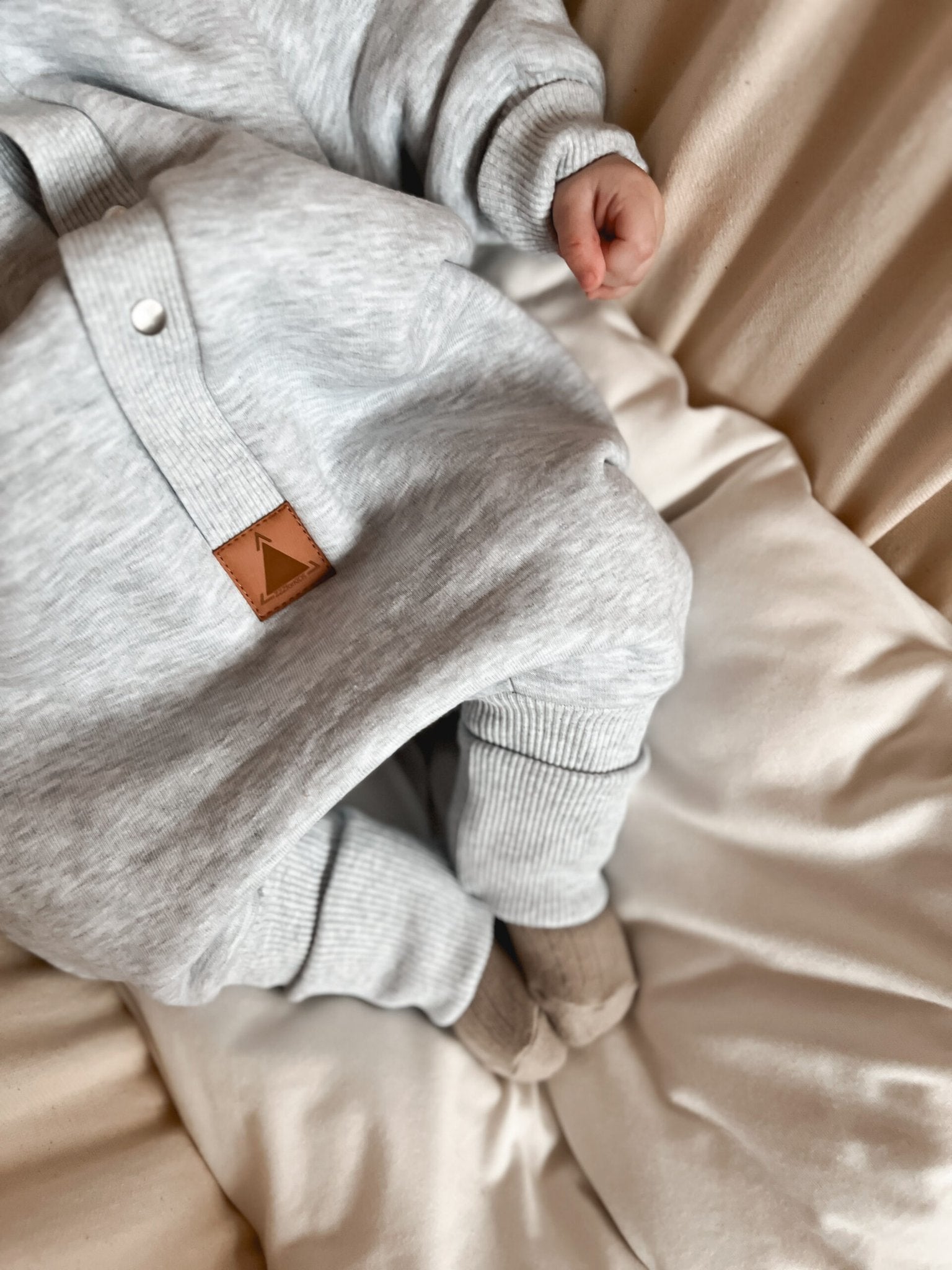 3. Close-up of Zezuzulla melange grey jumpsuit showing ribbed cuffs and leather logo patch