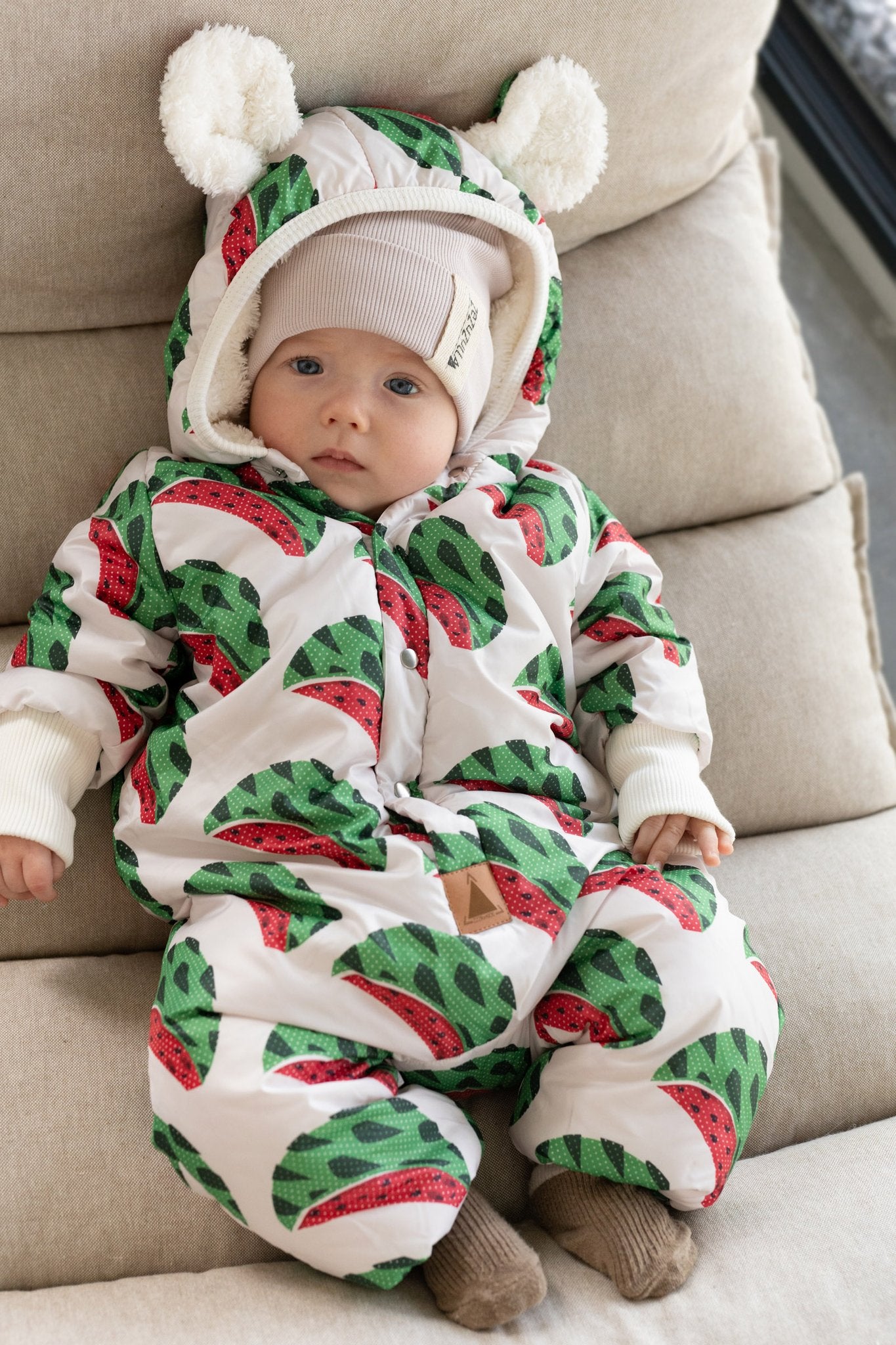 1. Baby wearing Zezuzulla winter jumpsuit with watermelon print and teddy ears hood, sitting on beige cushion