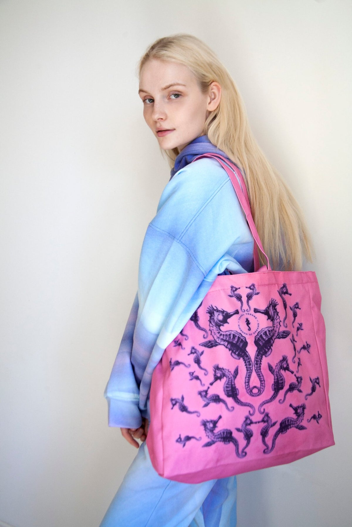 3. Woman holding pink Mirage tote bag with seahorse design, wearing blue and purple gradient outfit