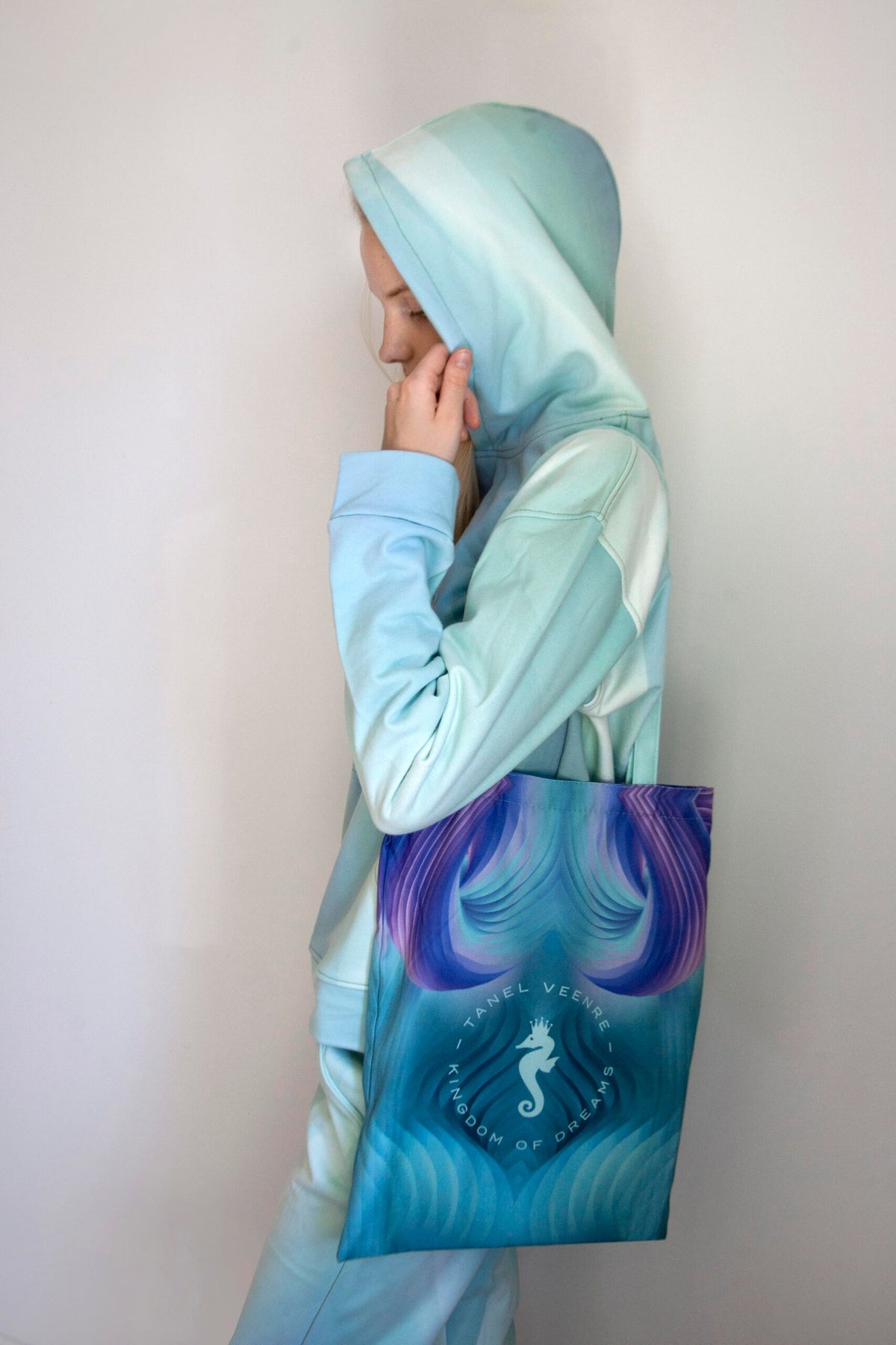 2. Woman in a pastel blue hoodie holding a Tanel Veenre Mirage tote bag with a seahorse design, shown in profile against a plain background