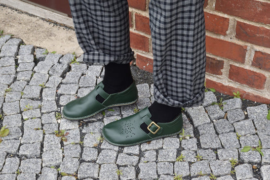 2. Women's Kuuda Shoes in dark green paired with a dress, highlighting elegant style while seated indoors