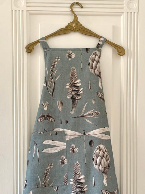 2. Hortensias Home Seeds Aqua apron with botanical print hanging on ornate hanger against white door