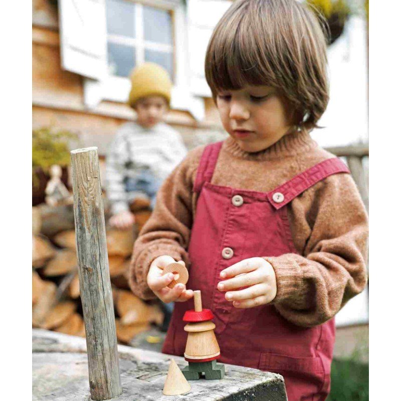 1. Child in red overalls assembling Wooden Story LALA Stick Figure Puzzle outdoors near a wooden house