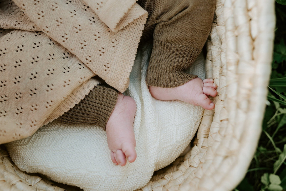 3. Close-up of baby's feet in brown romper under a beige merino wool blanket in a basket