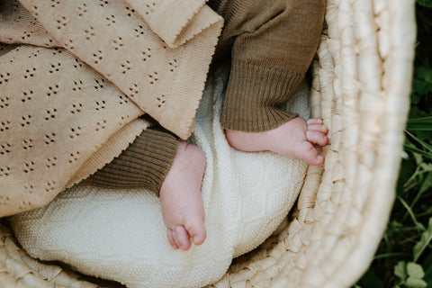 3. Close-up of baby's feet in brown romper under a beige merino wool blanket in a basket