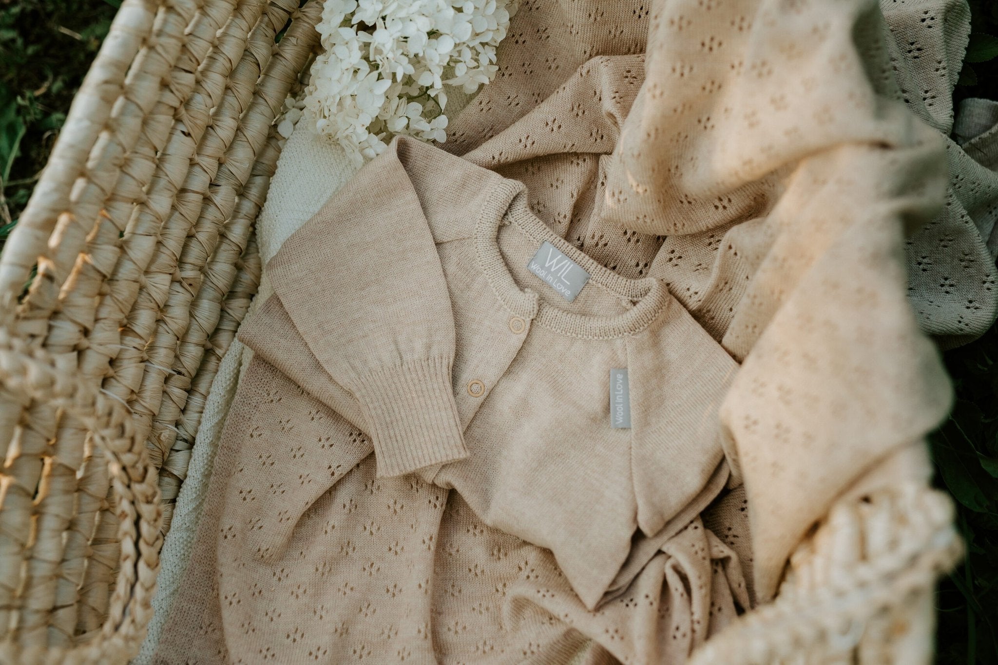 6. Beige merino wool baby romper and blanket with floral detail in a woven basket