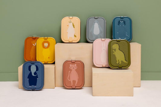 1. Collection of Trixie Baby lunch boxes with various animal designs displayed on wooden blocks against green background