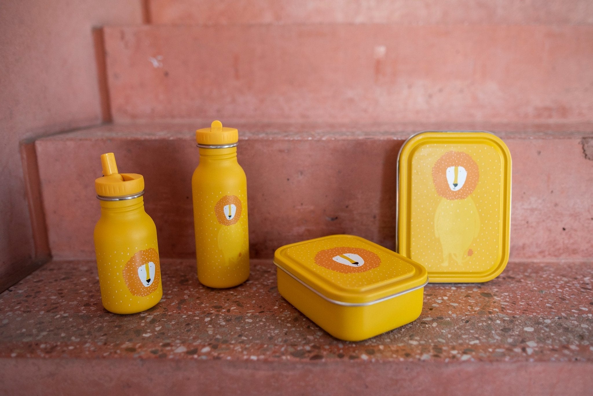3. Yellow Mr. Lion lunch box with matching bottles and larger lunch box on stone steps