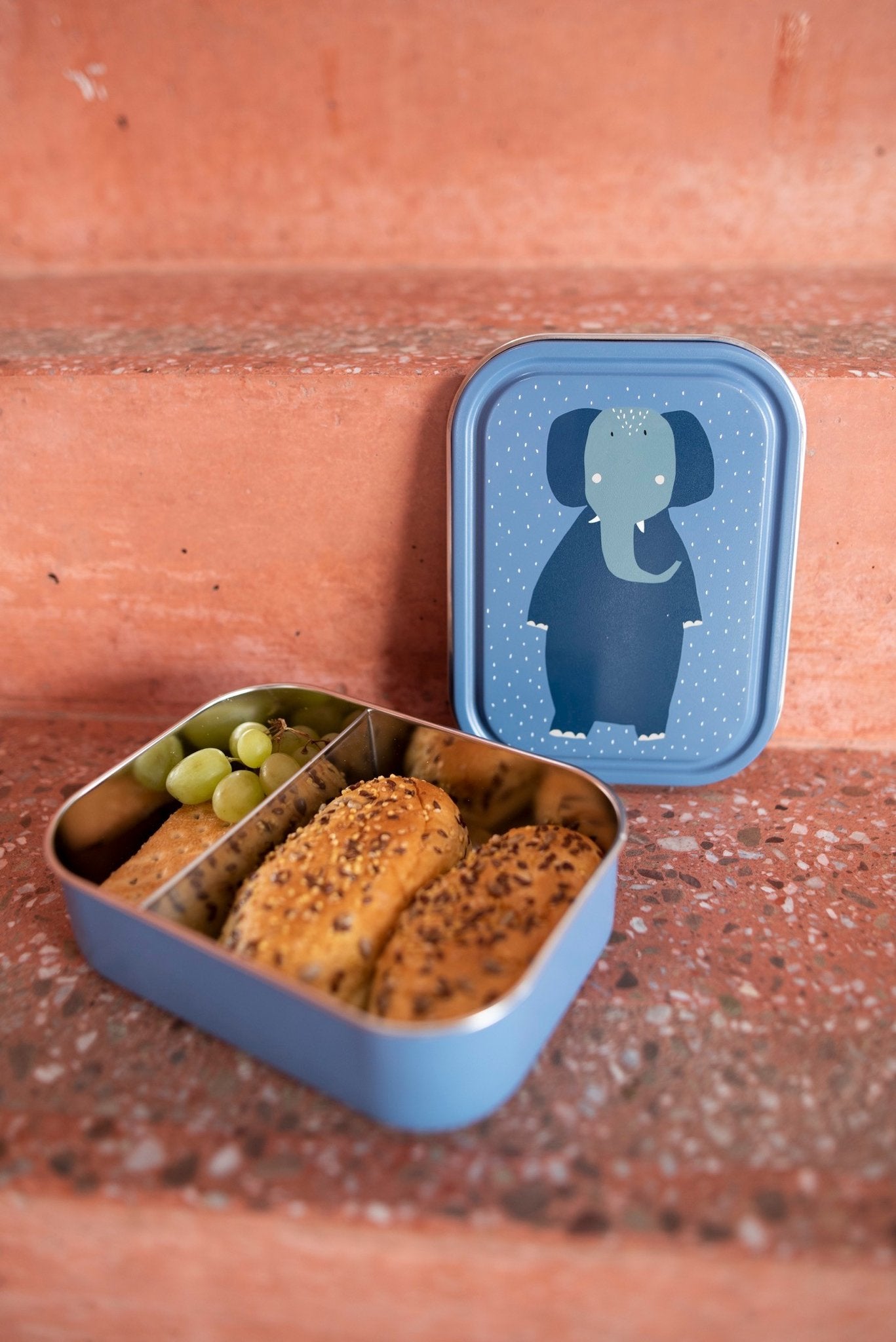 3. Open Trixie Baby Mrs. Elephant lunch box with snacks inside, placed on steps
