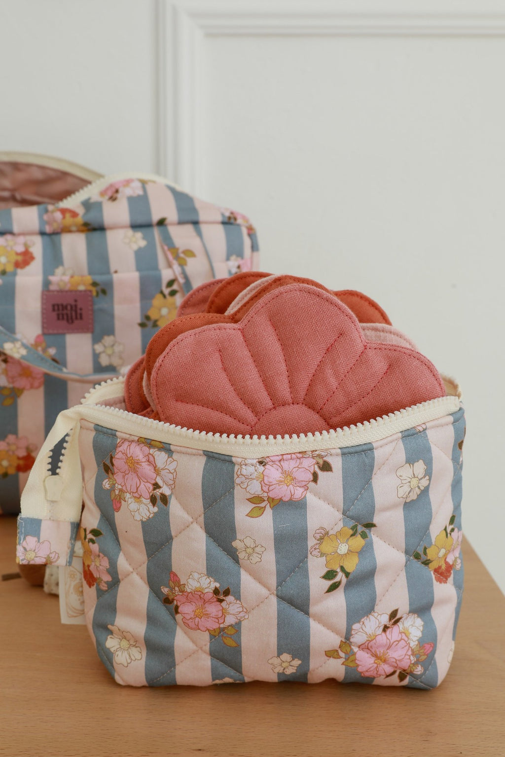 3. Quilted blue striped makeup bag with floral pattern, open to show pink quilted items inside, larger bag in background