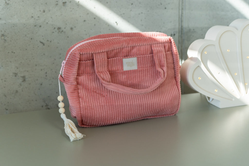 8. Coral makeup bag with tassel on dresser, next to shell lamp in natural light