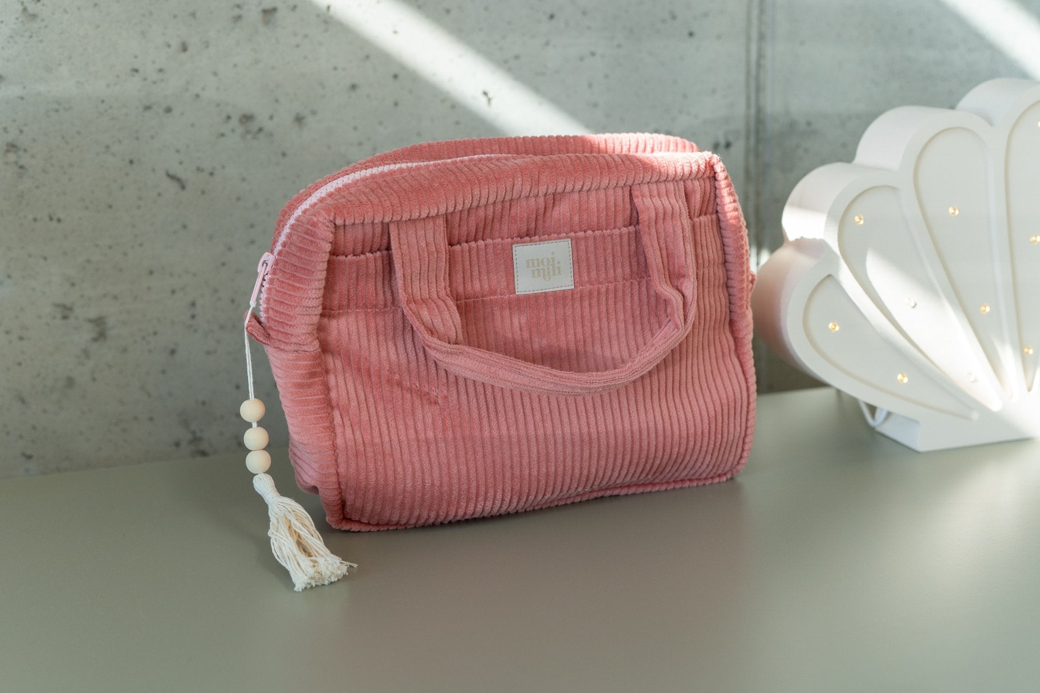 5. Large coral makeup bag with tassel detail on a light-colored surface with decorative elements