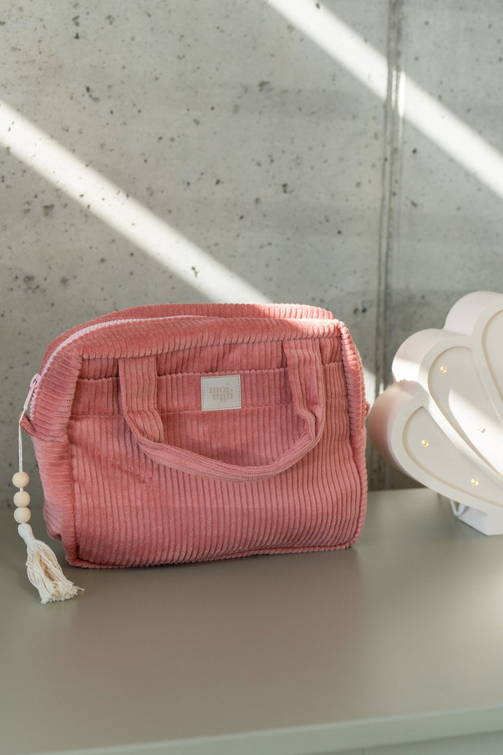 3. Coral makeup bag with tassel on dresser beside shell lamp, concrete wall background