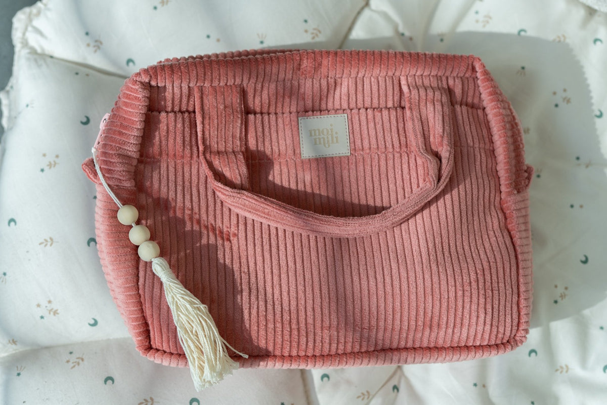1. Large coral makeup bag with handles and tassel detail, resting on a patterned cushion