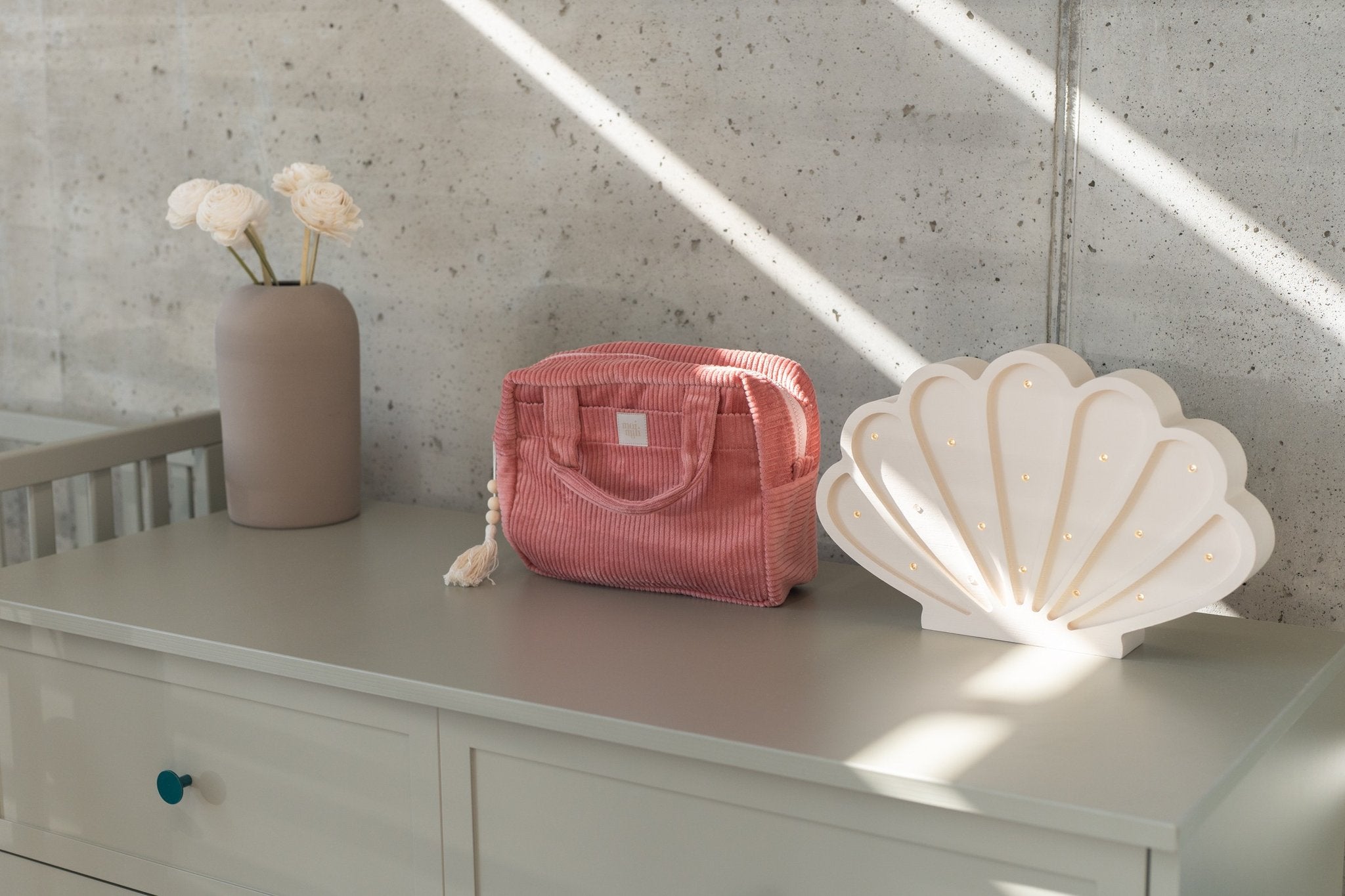 2. Coral makeup bag with tassel on dresser next to shell lamp and vase in natural light