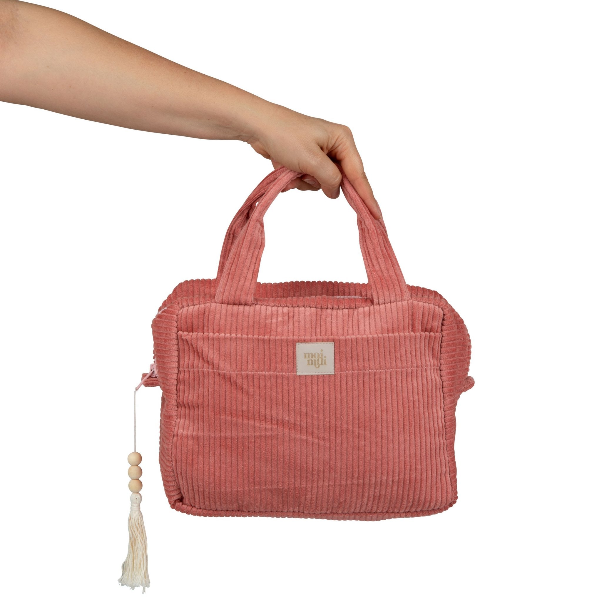 7. Hand holding coral makeup bag with tassel, showing Moi Mili logo