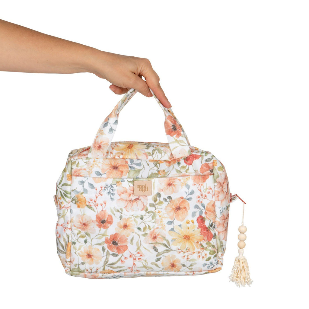 2. Hand holding Moi Mili large floral makeup bag with tassel, showing size and handle design