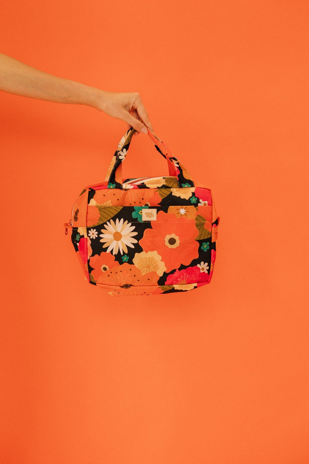 1. Hand holding large floral print makeup bag against orange background
