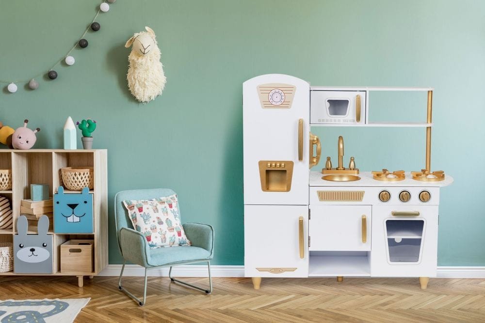 6. Angelove white and gold wooden play kitchen in a modern children's room with green wall