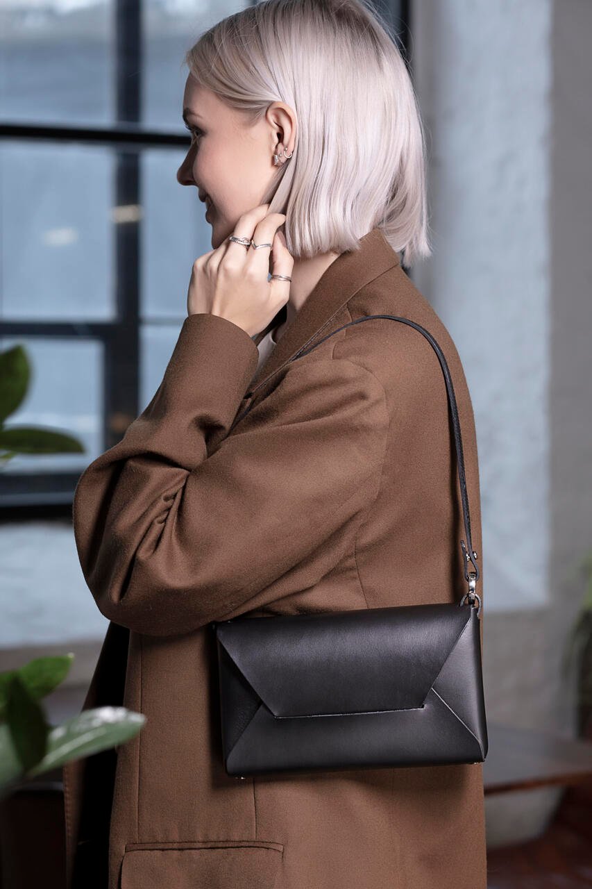 2. Woman in brown coat holding black Stella Soomlais Wine & Dine evening bag with shoulder strap in indoor setting