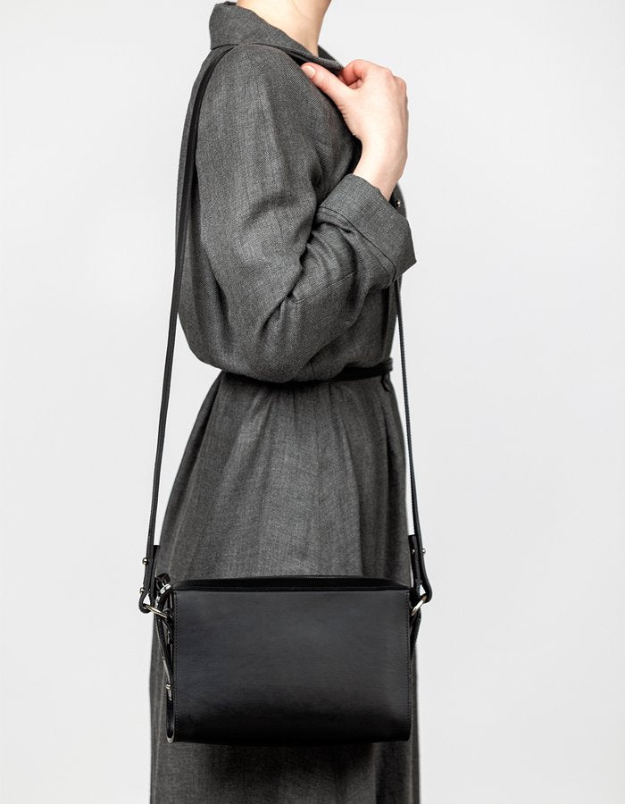 4. Woman wearing black Stella Soomlais Treasure Box handbag with long strap over shoulder, dressed in grey dress, studio setting