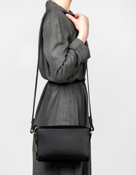 4. Woman wearing black Stella Soomlais Treasure Box handbag with long strap over shoulder, dressed in grey dress, studio setting