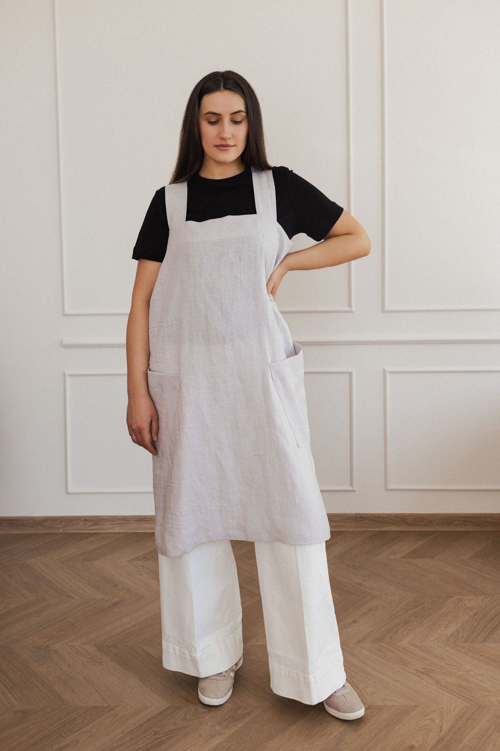 10. Woman in light grey linen apron with hand on hip, standing in a bright room