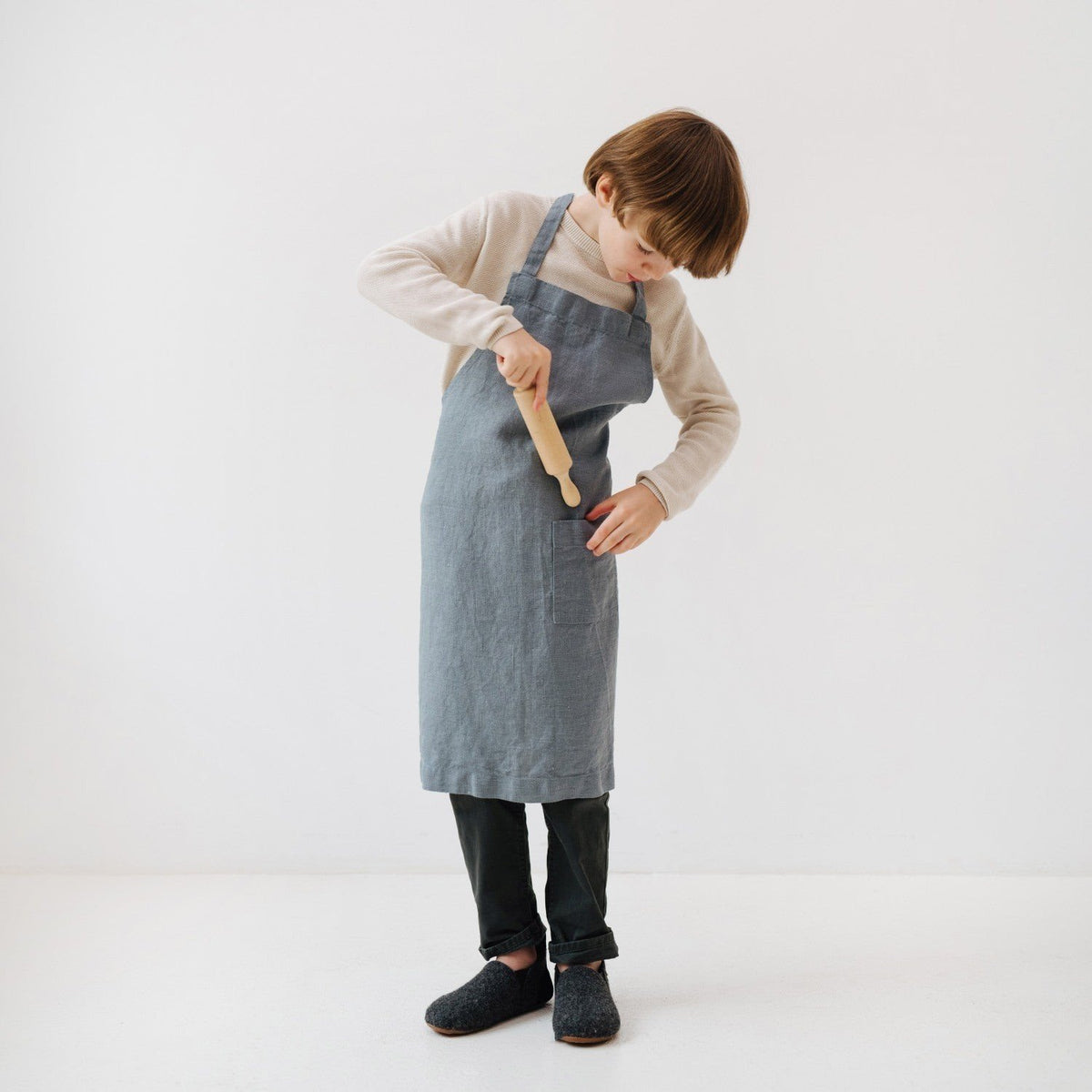 3. Child in blue fog linen apron using a wooden spoon, demonstrating apron functionality