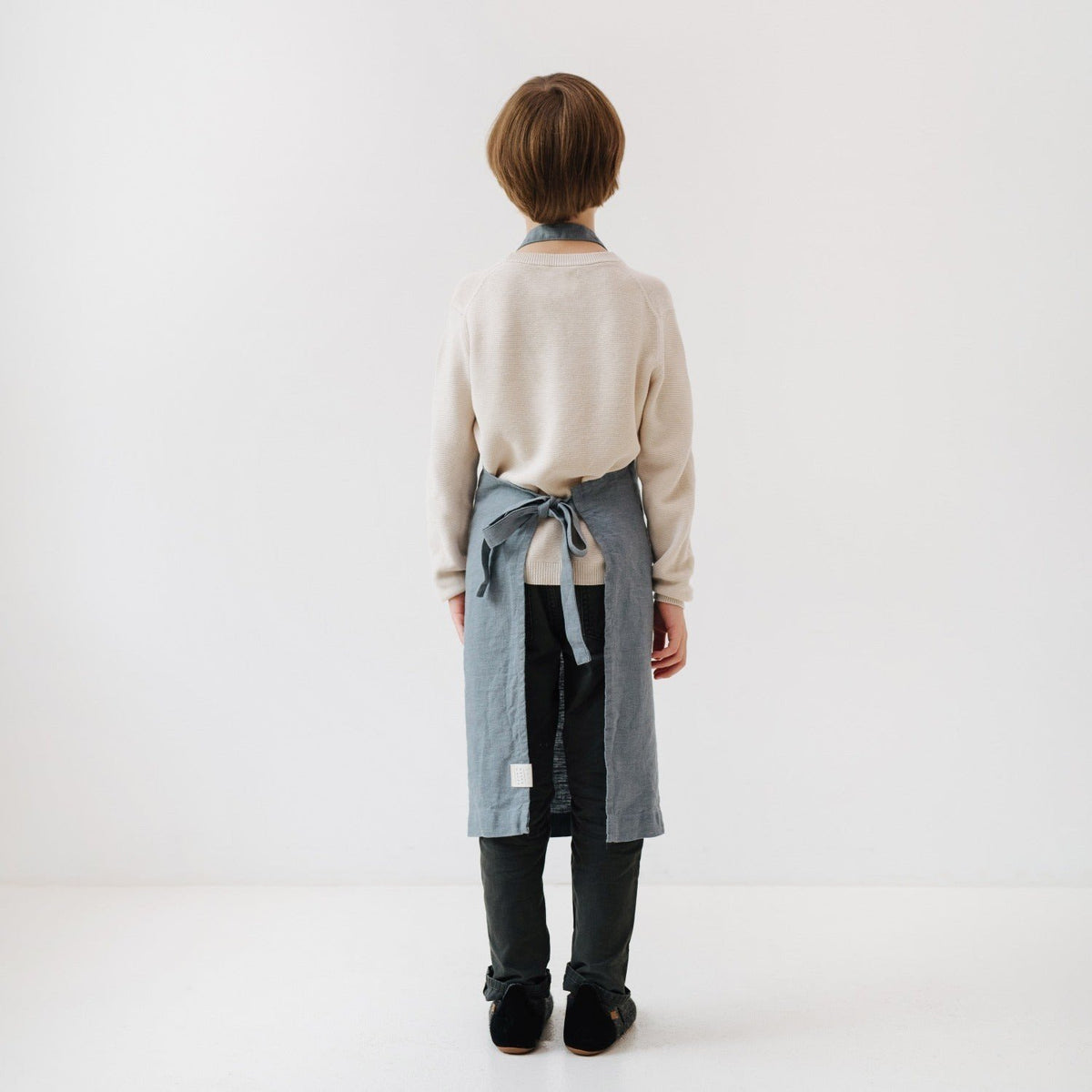 5. Back view of child in blue fog linen apron, highlighting tie closure and length