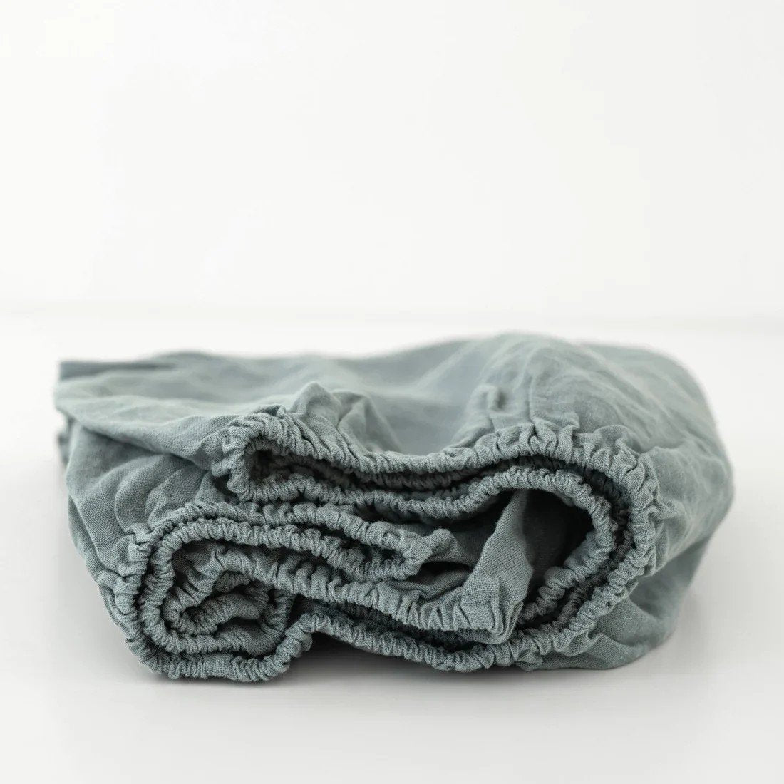 2. Blue fog linen fitted sheet for kids with elastic hem, folded on a white background, highlighting soft and durable fabric by Linen Tales.